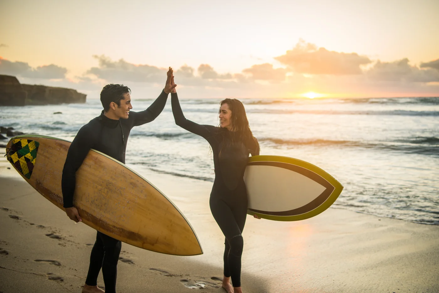 Two surfers celebrating on the beach at sunset